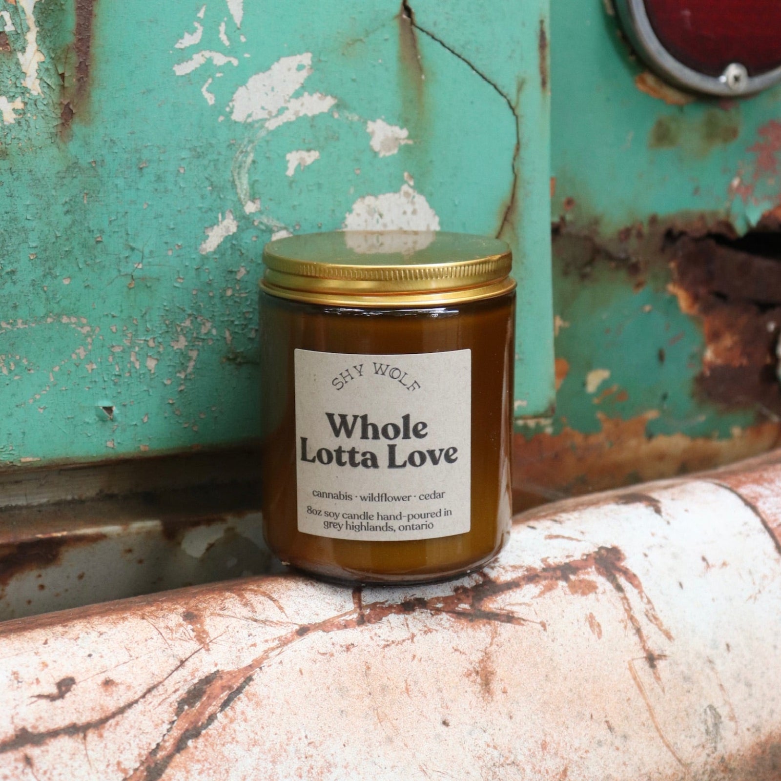 The Whole Lotta Love candle in front of a white and teal rusty background.