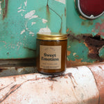 The Sweet Emotion candle in front of a white and teal rusty background.
