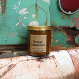 The Sweet Emotion candle in front of a white and teal rusty background.
