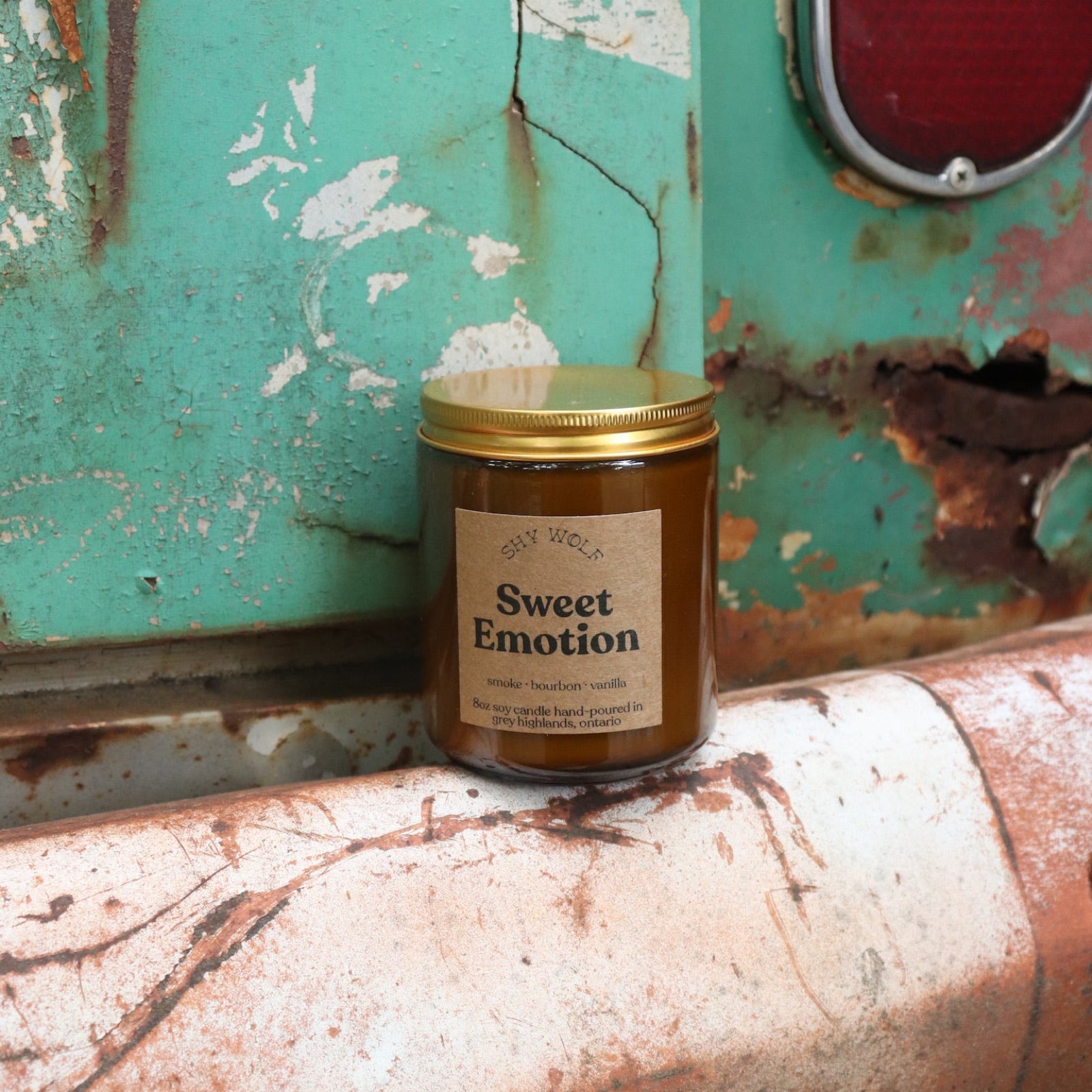 The Sweet Emotion candle in front of a white and teal rusty background.