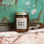 The Rebel Rebel candle in front of a white and teal rusty background.