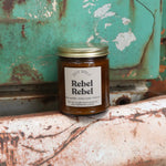 The Rebel Rebel candle in front of a white and teal rusty background.