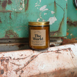 The World candle in front of a white and teal rusty background.