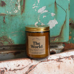 The World candle in front of a white and teal rusty background.