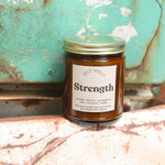 The Strength candle in front of a white and teal rusty background.