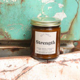 The Strength candle in front of a white and teal rusty background.