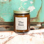 The Sun candle in front of a white and teal rusty background.