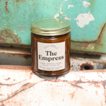 The Empress candle in front of a white and teal rusty background.