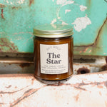 The Star candle in front of a white and teal rusty background.