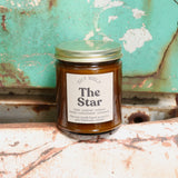 The Star candle in front of a white and teal rusty background.