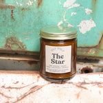 The Star candle in front of a white and teal rusty background.