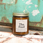 The Fool candle in front of a white and teal rusty background.