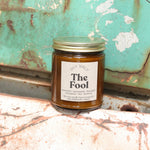 The Fool candle in front of a white and teal rusty background.