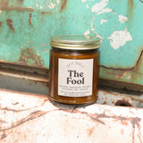 The Fool candle in front of a white and teal rusty background.