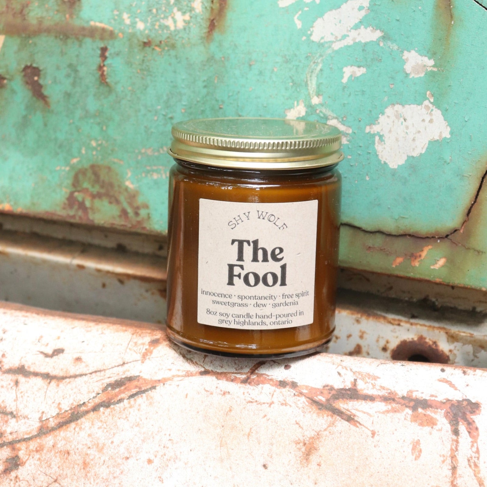 The Fool candle in front of a white and teal rusty background.