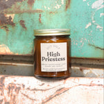 The High Priestess candle in front of a white and teal rusty background.