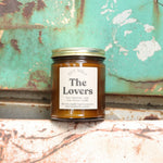 The Lovers candle in front of a white and teal rusty background.