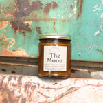 The Moon candle in front of a white and teal rusty background.