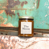 The Moon candle in front of a white and teal rusty background.