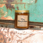 The Magician candle in front of a white and teal rusty background.