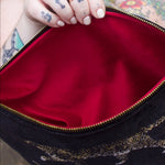 A woman holding the Black Velvet Leopard Traveller Large Pouch open to show off the red velvet lining.