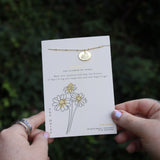 Someone holding the daisy 14k Gold Dipped Nickel-Free Birth Month Flower Necklace in front of greenery.