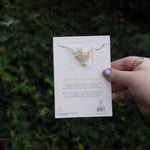 Someone holding the daisy 14k Gold Dipped Nickel-Free Birth Month Flower Necklace in front of greenery showing off the back.