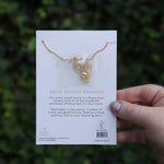 Someone holding the peony 14k Gold Dipped Nickel-Free Birth Month Flower Necklace in front of greenery showing off the back.