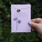 Someone holding the chrysanthemum 14k Gold Dipped Nickel-Free Birth Month Flower Necklace in front of greenery.