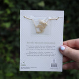 Someone holding the holly 14k Gold Dipped Nickel-Free Birth Month Flower Necklace in front of greenery showing off the back.