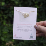 Someone holding the rose 14k Gold Dipped Nickel-Free Birth Month Flower Necklace in front of greenery showing off the back.