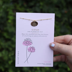 Someone holding the lotus 14k Gold Dipped Nickel-Free Birth Month Flower Necklace in front of greenery.