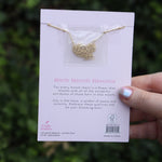 Someone holding the lotus 14k Gold Dipped Nickel-Free Birth Month Flower Necklace in front of greenery showing off the back.