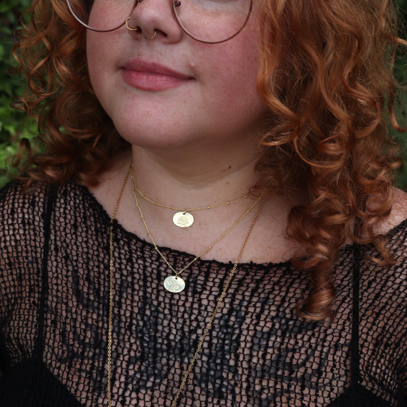 A woman wearing two of the 14k Gold Dipped Nickel-Free Birth Month Flower Necklaces with a black mesh top.