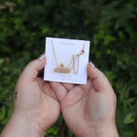 Someone holding the Tiny Turquoise Moon Necklace in front of greener showing off the back.
