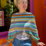 Someone wearing the coffee Vintage Rainbow Hollow Knit Sweater in front of an orange and pink wall with a window.