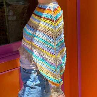 Someone wearing the coffee Vintage Rainbow Hollow Knit Sweater in front of an orange and pink wall with a window.