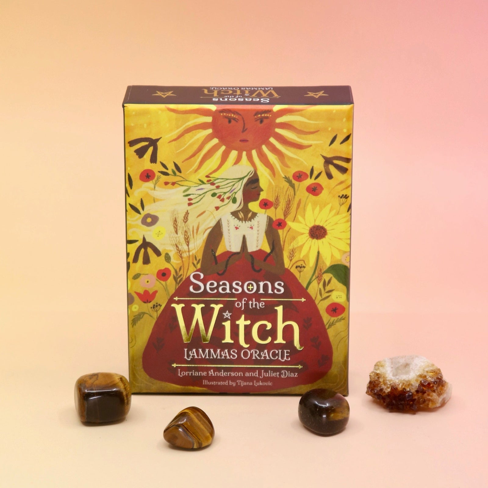 The Lammas Oracle Card Deck surrounded by tumbled crystals on a pink and yellow background.