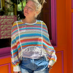 Someone wearing the white Vintage Rainbow Hollow Knit Sweater in front of an orange and pink wall with a window.