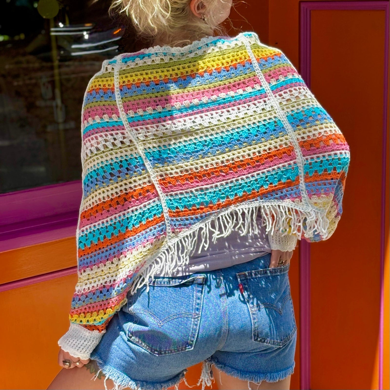 Someone wearing the white Vintage Rainbow Hollow Knit Sweater in front of an orange and pink wall with a window.