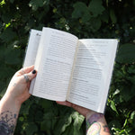 Someone holding one of the books open from the Witchcraft Boxed Set by Arin Murphy-Hiscock in front of greenery.