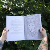 Someone holding the Tarot Coloring - Coloring Book open in front of greenery showing off pages.