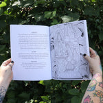 Someone holding the Tarot Coloring - Coloring Book open in front of greenery showing off pages.