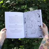 Someone holding the Tarot Coloring - Coloring Book open in front of greenery showing off pages.