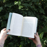 Someone holding the Green Witch by Arin Murphy-Hiscock open in front of greenery, showing off the pages.