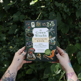 Someone holding the Green Witch's Sticker Book by Arin Murphy-Hiscock in front of greenery.