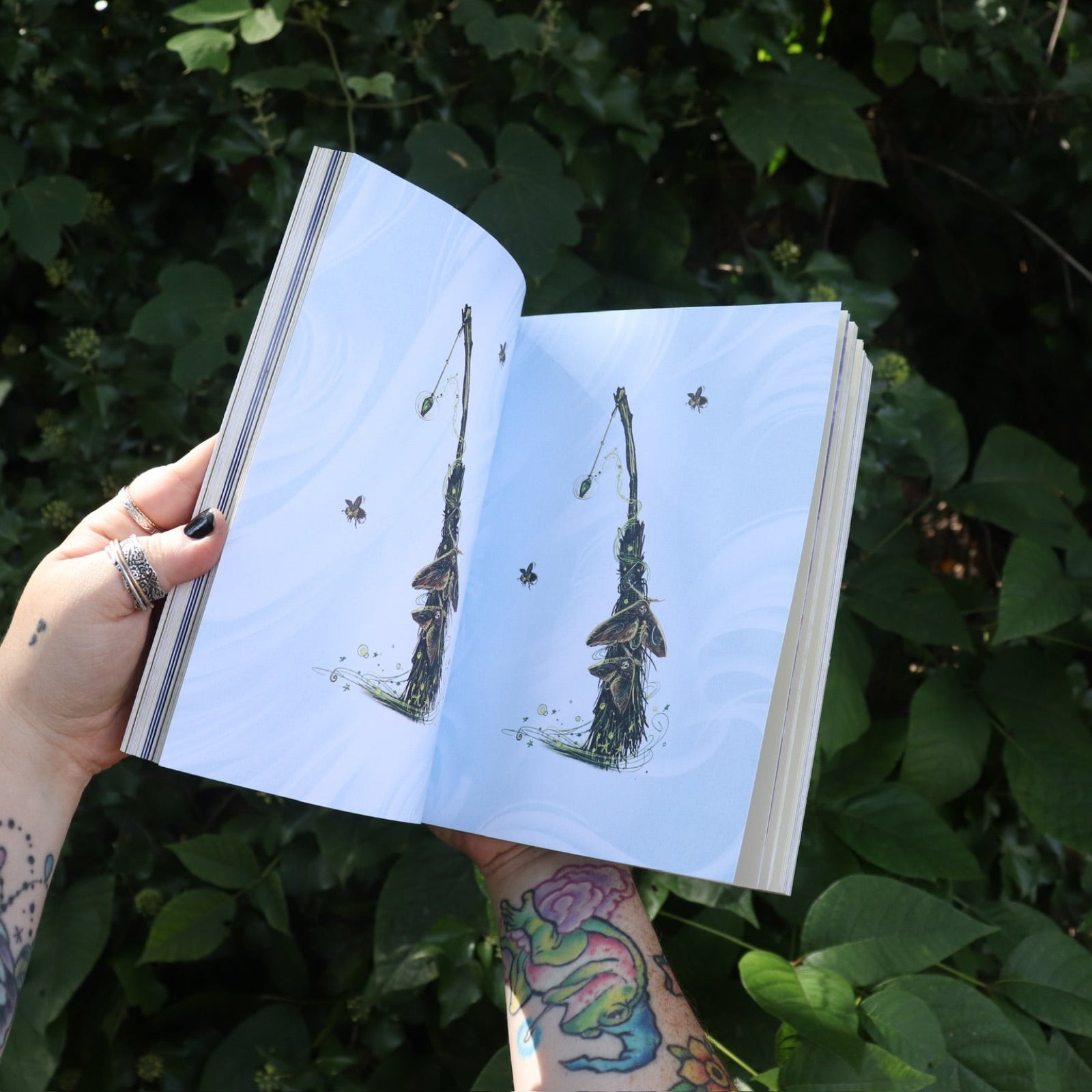 Someone holding the Green Witch's Sticker Book by Arin Murphy-Hiscock open in front of greenery, showing odd the sticker pages.