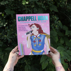 Someone holding the Chappell Roan Coloring & Activity Book in front of greenery.