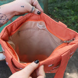 A woman holding the Daisy Embroidered Orange Linen Zipper Tote Bag open showing off the inside.