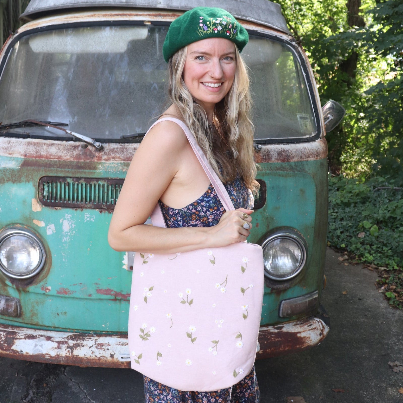 A woman wearing a navy floral dress has the Daisy Embroidered Pastel Pink Linen Zipper Tote Bag on her shoulder.